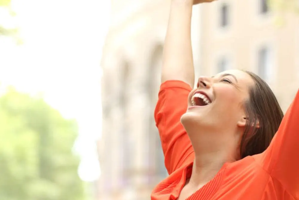 A joyful woman outdoors with her arms raised in the sunshine