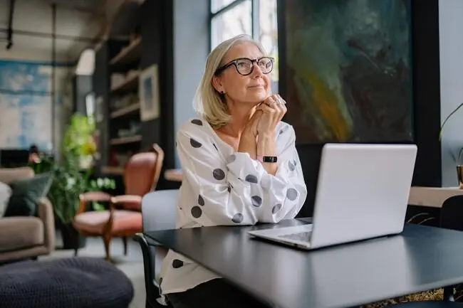 A woman sitting thoughtfully at a table with her laptop