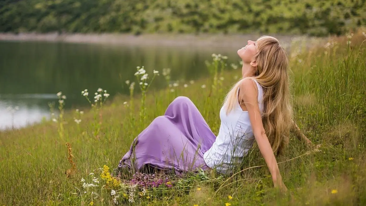 A woman resting in a meadow beside a lake