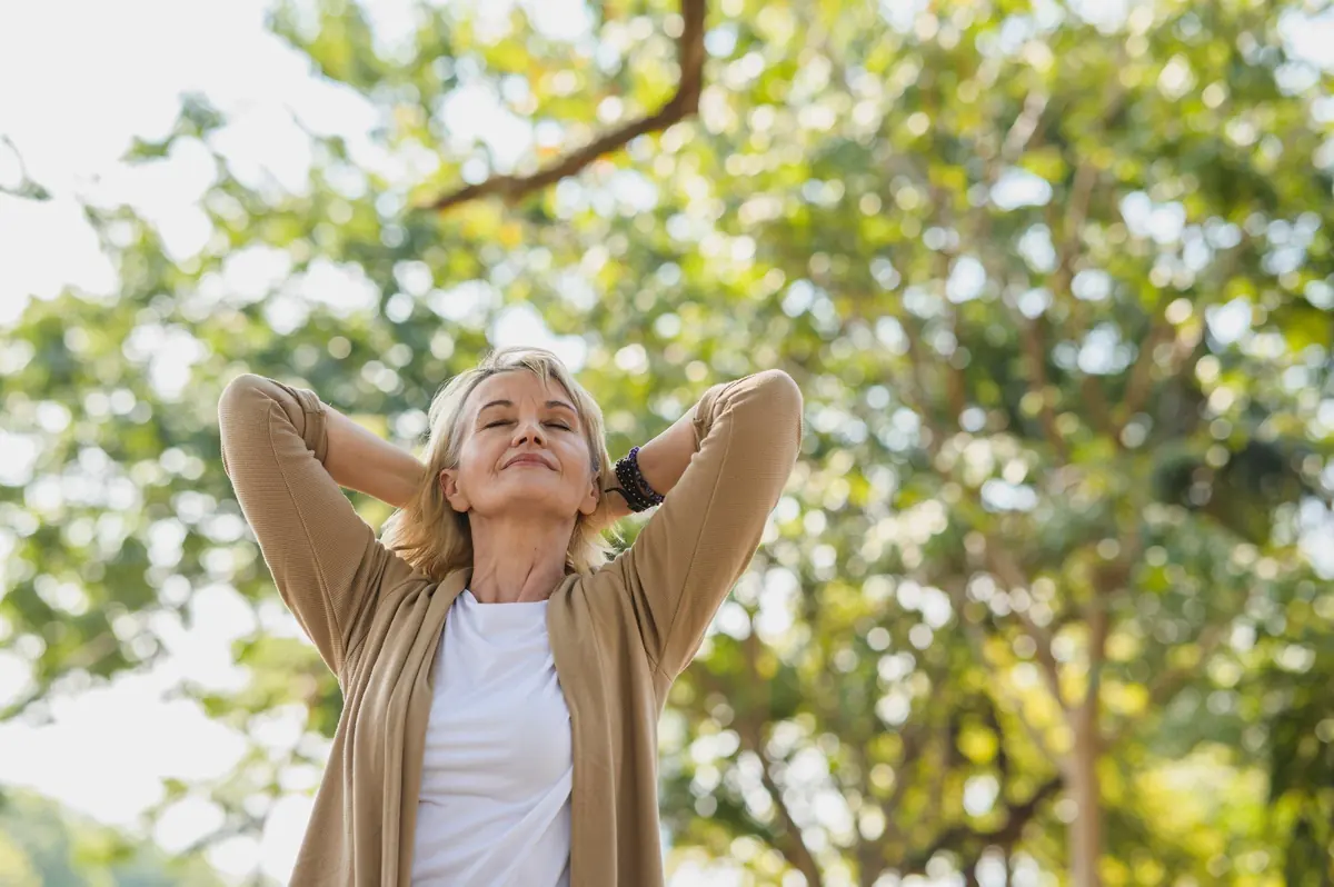 A woman stretching outdoors under green trees